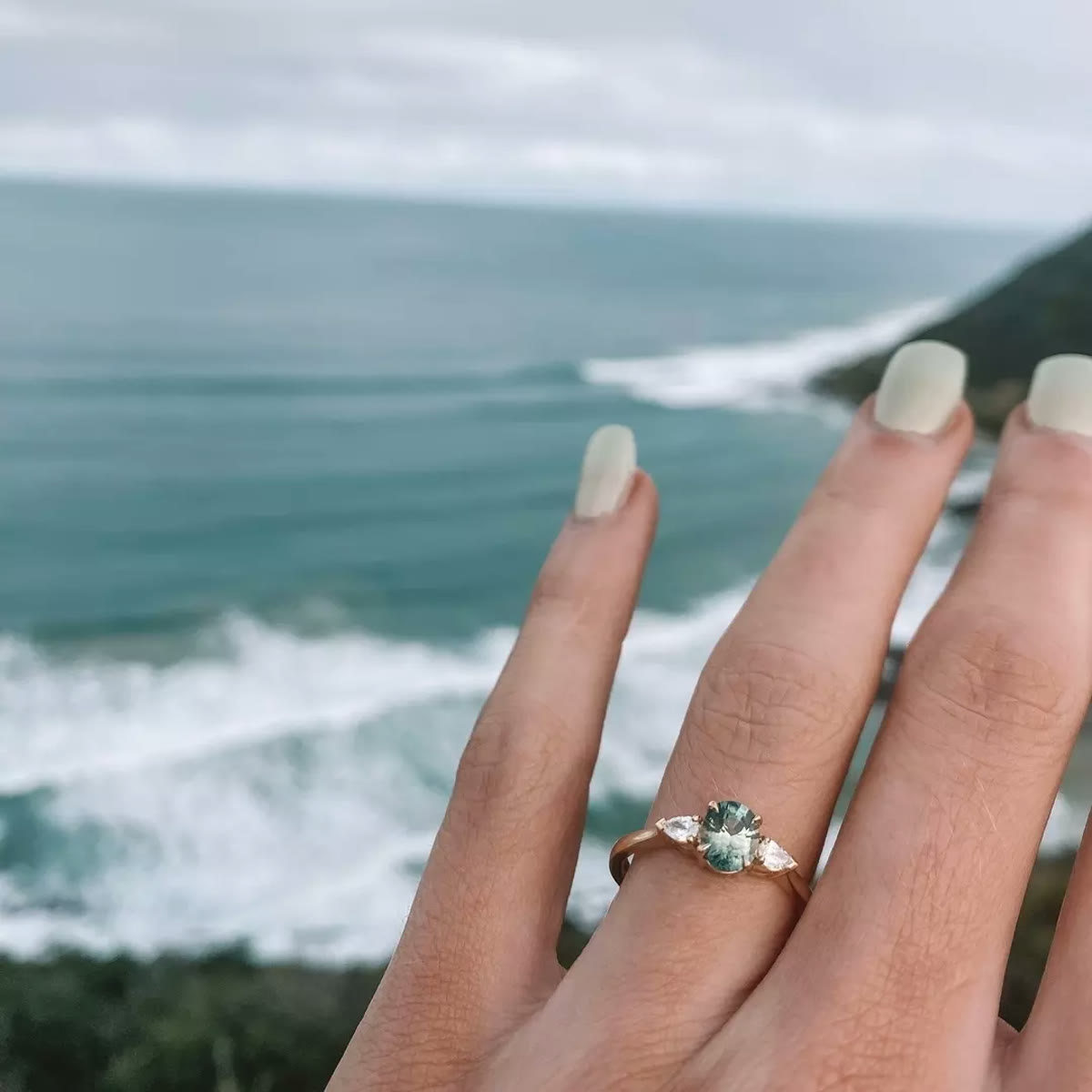 Green sapphire engagement ring photographed above the ocean